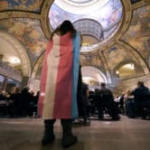 A person stands in the Missouri Statehouse with a transgender flag draped over them.