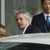 Two Asian men stand near William Burns as he enters a car at Capital International Airport in Beijing.