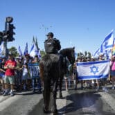 A police officer on a horse monitors a crowd of protesters, many of them holding the flag of Israel.