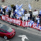 People hold signs and Israeli flags while protesting Benjamin Netanyahu on a sidewalk in Fremont, California.