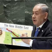 Benjamin Netanyahu draws a red line through a placard with a map of North Africa and the Middle East while giving a speech.