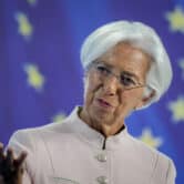 Christine Lagarde raises her right hand while speaking on stage an event.