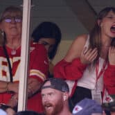A woman wearing a red, number 87 Kansas City Chiefs jersey stands to Taylor Swift and several other people in a private suite at Arrowhead Stadium.