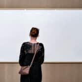 A person wearing a purse looks at an empty picture frame titled "Take the Money and Run" at an art museum.