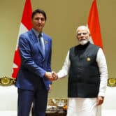 Justin Trudeau and Narendra Modi shake hands while posing for photos in front of their respective flags.