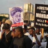 A group of people gather during a protest, with two of them holding signs referencing the mysterious death of Mohbad, in a street in Lagos, Nigeria.