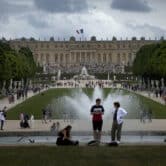 Visitors walk around the Chateau de Versailles gardens, with the Palace of Versailles in the background.