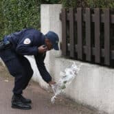 A French police officer lays flowers against a wall on a sidewalk.