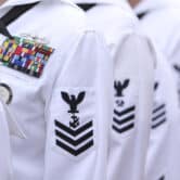 Five U.S. sailors wearing white uniforms line up.
