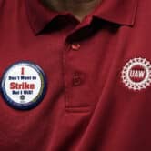 Shawn Fain wears a button on his red UAW collared shirt that reads "I don't want to strike but I will!"