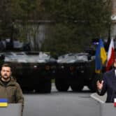 Volodymyr Zelenskyy and Mateusz Morawiecki stand behind podiums during a news conference, with tanks in the background.
