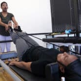 A health care worker helps a patient lying on a Pilates machine.
