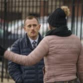 A person gestures while speaking to Josh Kruger near a parking lot.