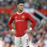 Ronaldo stands on the pitch while wearing a primarily red and white Manchester United uniform during a soccer match at Old Trafford stadium.