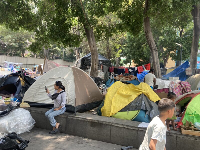 A woman looks at her telephone on the right at a migrant encampment in Mexico City.