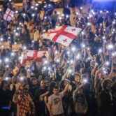 A large group of people holding flags and cellphone flashlights.