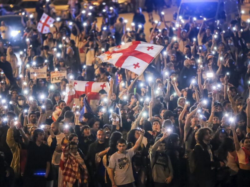 A large group of people holding flags and cellphone flashlights.
