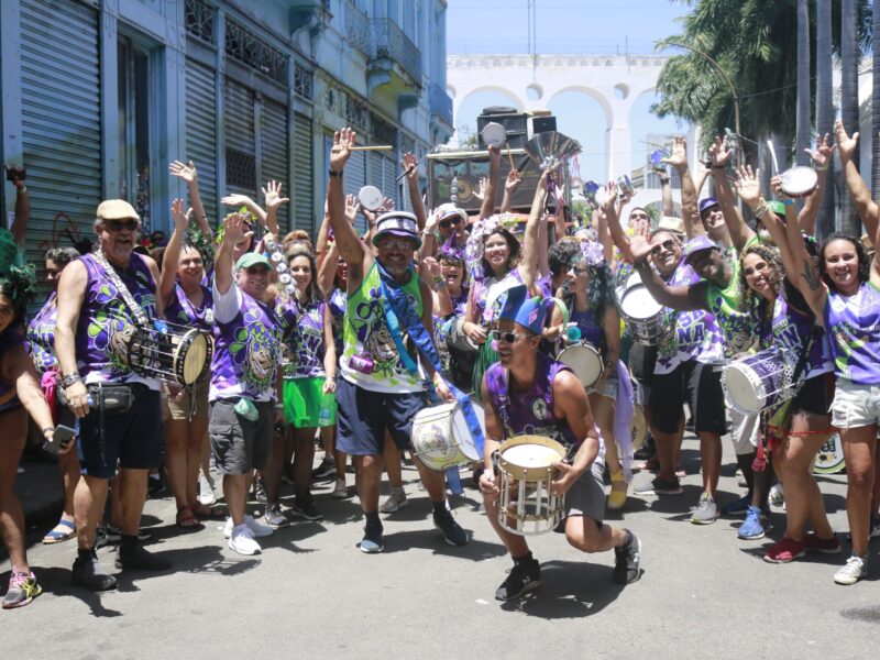 Carnival revelers celebrate in vibrant costumes with the iconic Arcos da Lapa in the background.