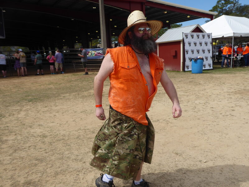A man with a orange shirt and camo kilt