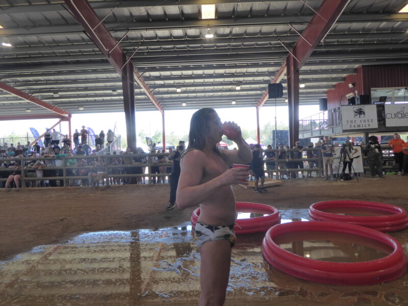 A man in a speedo drinks bong water and whiskey as part of a game
