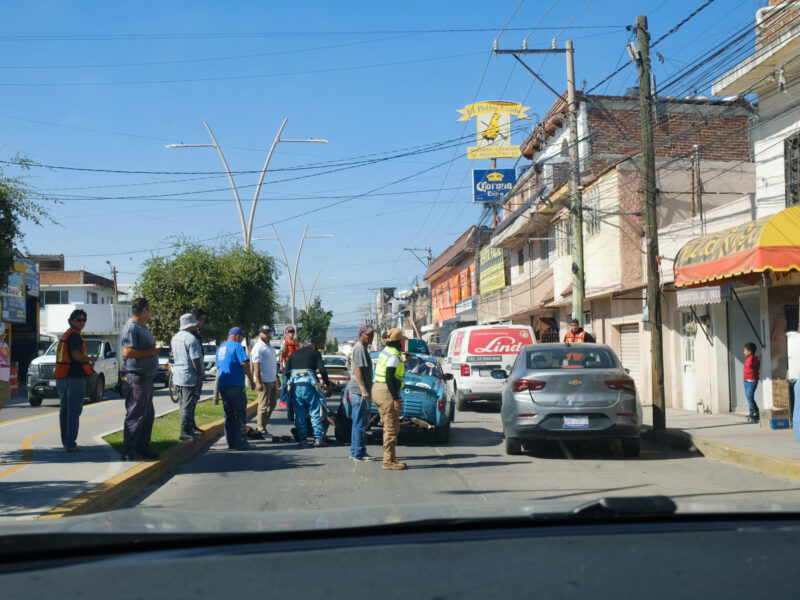 A blue car in the middle of a road in front of a chicken restaurant broken down in Mexico.