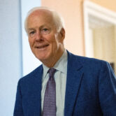 Sen. John Cornyn walks through a hallway in the U.S. Capitol, wearing a blue suit and patterned tie.