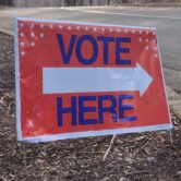 A red “Vote Here” sign with an arrow points toward an early voting location outside Lake Lynn Community Center in Raleigh, North Carolina.