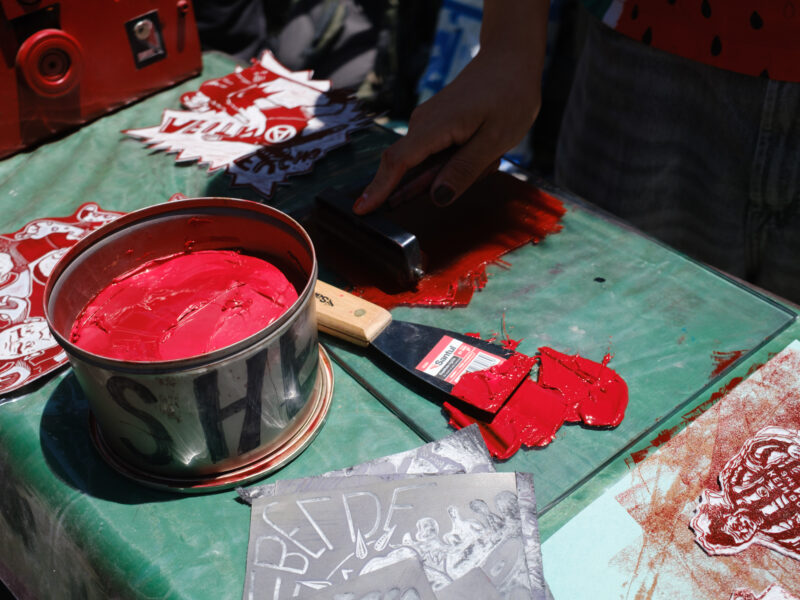 A red paint brush sits on a green table with molds for printmaking. 