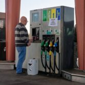 A man with a jerry can stands at an automated gas pump with a handmade sign.