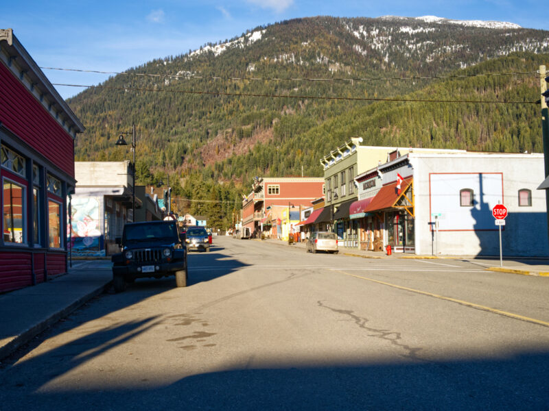A small town street with storefronts and mountains in the background.
