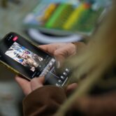 A girl with long blond hair edits a video of herself on a cell phone.