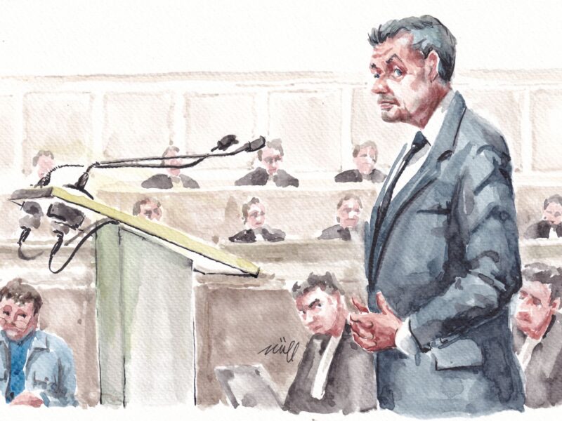 A watercolor of Nicolas Sarkozy standing to testify as a jury and lawyers look on.