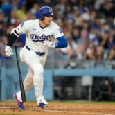 A baseball player in a Dodgers uniform sprints toward first base as his bat falls behind him.
