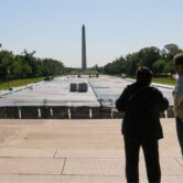Tourists look out onto empty reflecting pool