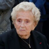 Elderly woman in black attire attends a ceremony in Paris.