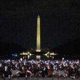 A large crowd gathers in front of the Lincoln Memorial Reflecting Pool at night, reacting during a UFC news conference with the illuminated Washington Monument rising in the background.