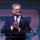 Xavier Becerra stands at a podium and applauds while speaking at an election night event in Los Angeles.