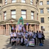 "Save Lloyd" protesters pose outside Portland City Hall with a large puppet called "Lloydalina" and signs supporting the Lloyd neighborhood.