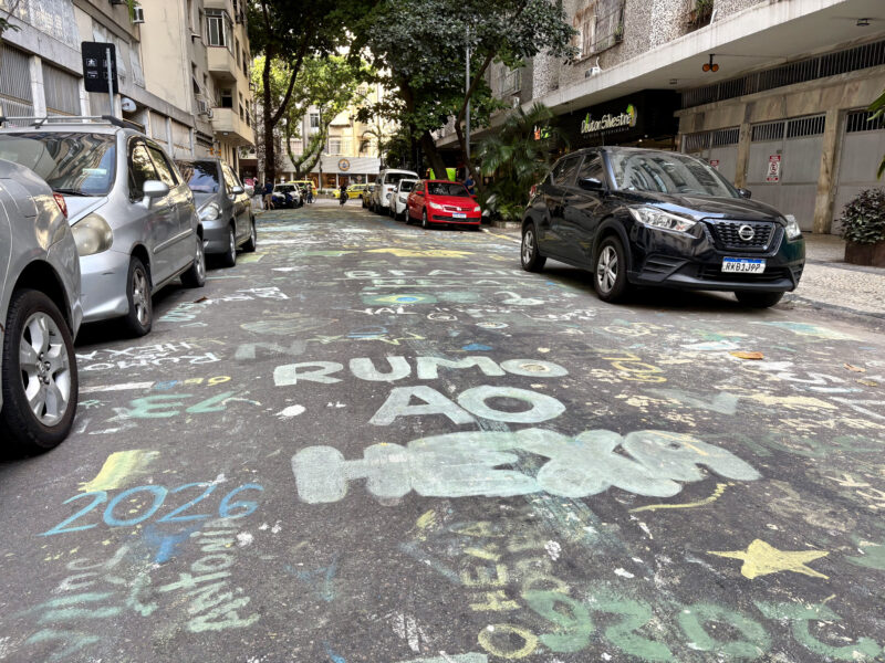 A Rio de Janeiro street is covered with faded green, yellow and blue World Cup drawings, including the phrase 