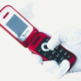 A right hand in a white glove holds an open red flip phone against a white background.