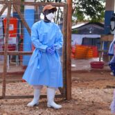 A health worker in protective gear stands outside an Ebola treatment center as residents watch in Bunia, Congo.