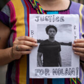 A person holds a handmade sign with a photo of Nolan Xavier Wells that reads, “Justice for Nolan!”