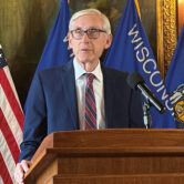 Wisconsin Gov. Tony Evers speaks at a podium during a news conference with U.S. and Wisconsin flags behind him.