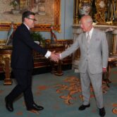 Andy Burnham smiles as he shakes King Charles' hand in a room with ornate furnishings and a decorated carpet.