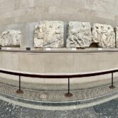 A museum display of friezes along a curved wall with a tiled floor.