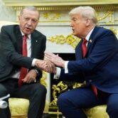 Erdogan and Trump sit in gold armchairs and shake hands.