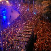 A large crowd of people packed in an outdoor space with a metal structure under streetlights.